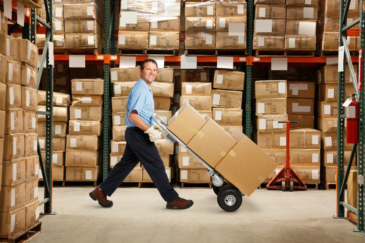 Warehouse worker pushing hand truck with boxes.