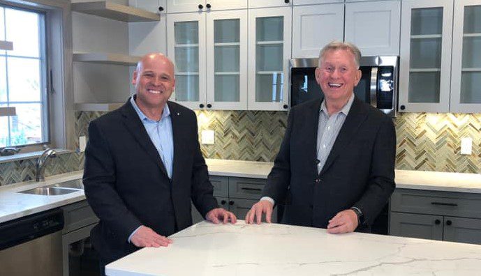 Image shows two men standing behind a kitchen counter