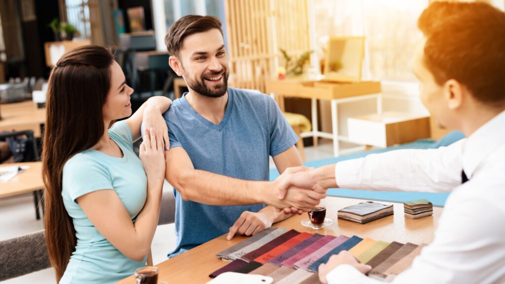 Man and woman buying making a furniture deal with a salesman and shaking hands.