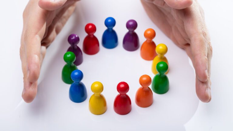 Person's Hand Protecting Multi Colored Pawns Forming Circle Over White Desk