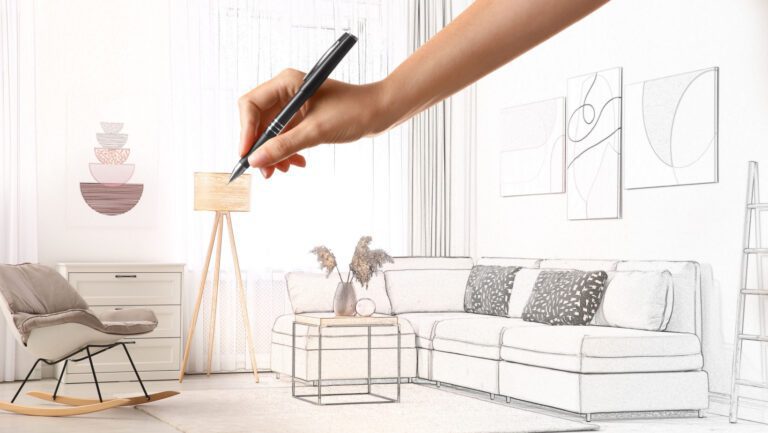A hand holding a pencil sketching furniture in a room on a pad.