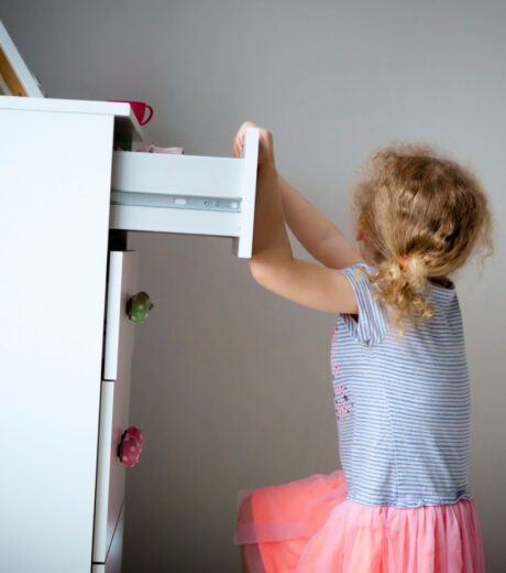 Young girl child climbing on modern high dresser furniture, danger of dresser dipping over concept. Children home hazards.