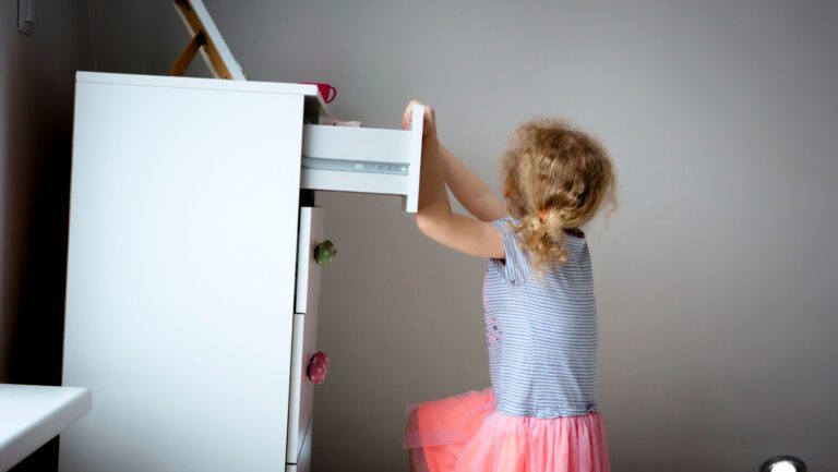 Young girl child climbing on modern high dresser furniture, danger of dresser dipping over concept. Children home hazards.