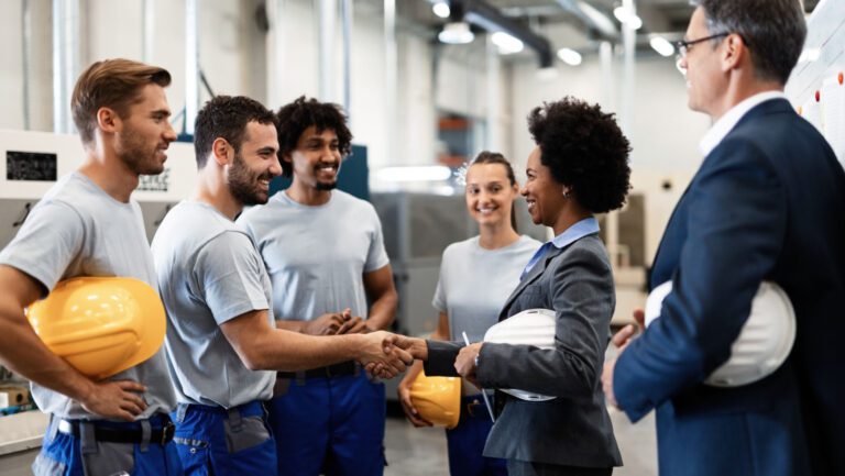 Happy manual worker handshaking with African American manager who is visiting factory with her colleague.