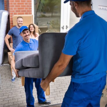 Happy Family Couple Watching Movers Unload Furniture From Truck