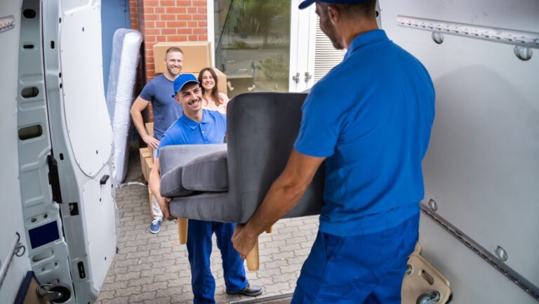 Happy Family Couple Watching Movers Unload Furniture From Truck