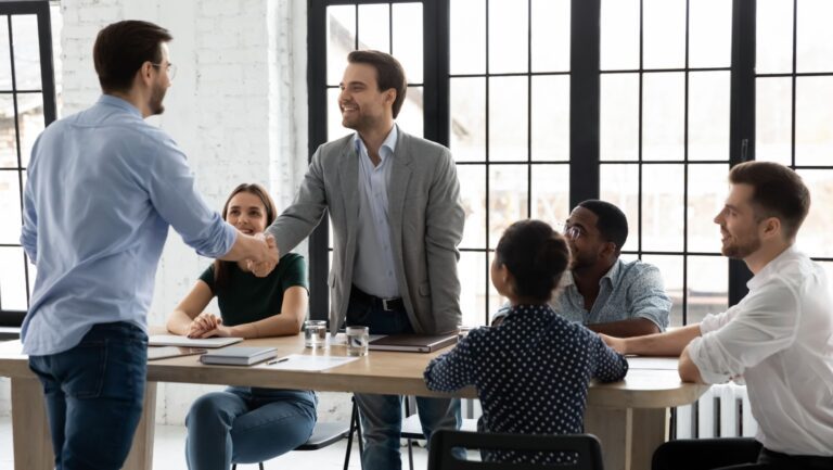 Greetings, you are hired! Smiling boss leader shaking hand of new team member student intern recruiting him for job on staff briefing, satisfied ceo appreciating male employee for perfect task result