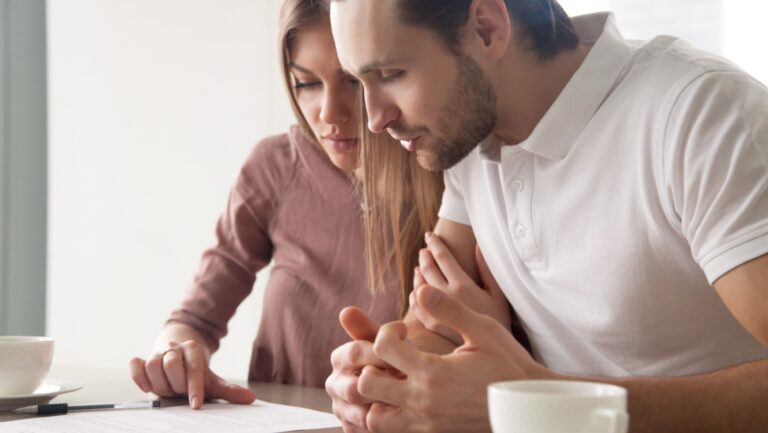 Serious couple studying contract agreement, reading terms and conditions attentively before signing, husband and wife calculating domestic bills, considering mortgage loan offer, health insurance