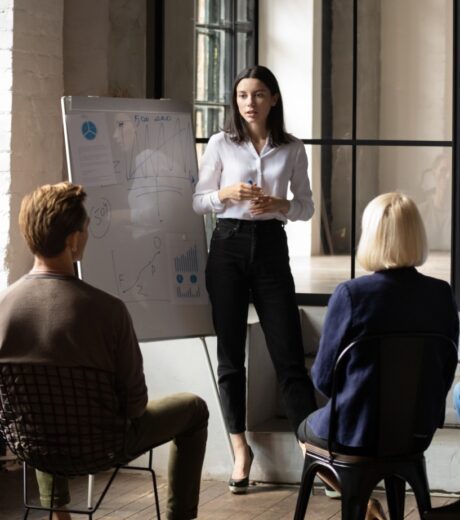 Confident lady sales coach leader give flip chart presentation consulting clients teaching employees training team people speaking explaining strategy at marketing workshop concept