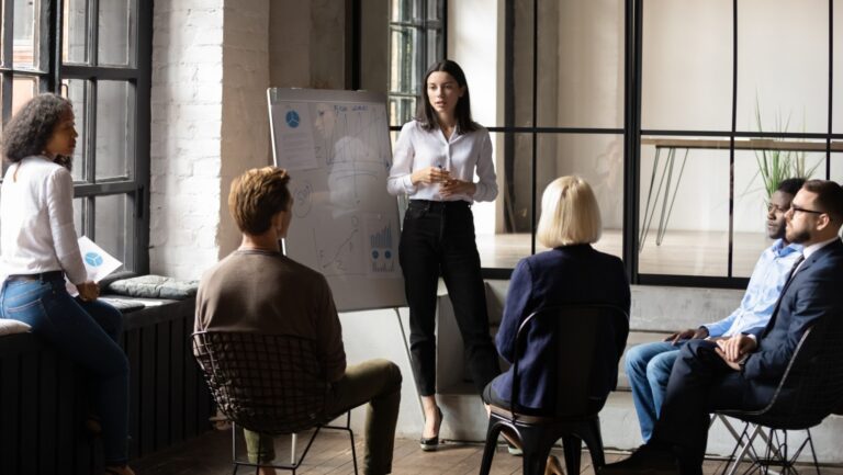 Confident lady sales coach leader give flip chart presentation consulting clients teaching employees training team people speaking explaining strategy at marketing workshop concept
