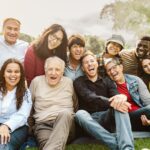 Happy multigenerational people having fun sitting on grass in a public park - People diversity concept
