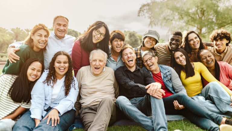 Happy multigenerational people having fun sitting on grass in a public park - People diversity concept