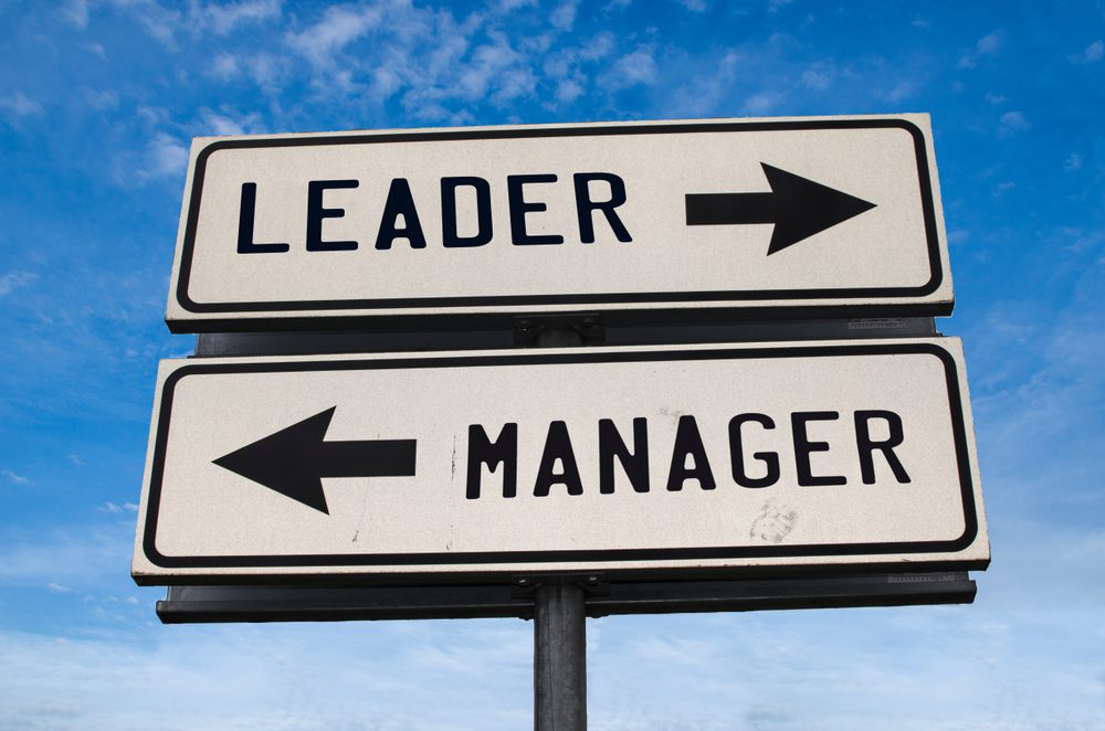 Leader vs manager. White two street signs with arrow on metal pole with word Leader and Manager. Directional road. Crossroads Road Sign, Two Arrow. Blue sky background.