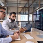Two marketing managers discussing marketing POS data reports on a computer looking at screen