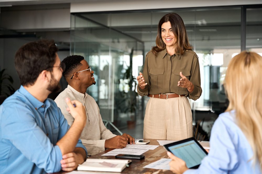 Happy middle aged business woman executive ceo leader discussing project management planning strategy working with diverse colleagues company team at office corporate board group meeting