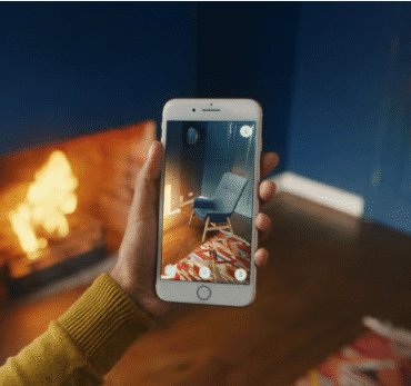 Female hand holding phone that shows 3D image of chair. Fireplace in the background