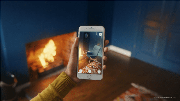 Female hand holding phone that shows 3D image of chair. Fireplace in the background