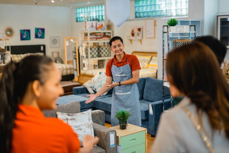 shop assistant man invites customers to see furniture products when customers arrive at the store