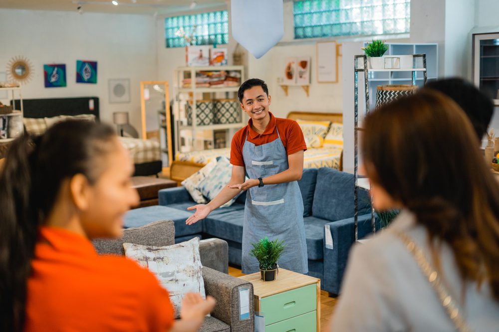 shop assistant man invites customers to see furniture products when customers arrive at the store