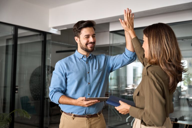 Happy smiling executive business team two partners employees giving high five celebrating professional corporate success, leadership or financial work achievement standing in office.