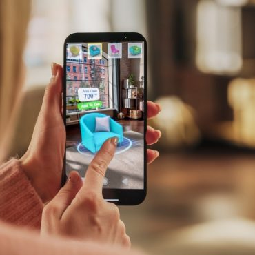 Decorating Apartment: Woman Holding Smartphone, using Augmented Reality Interior Design Software Chooses 3D Furniture for Home. Pick a Stylish Chair for the Living Room. Over Shoulder Close-up Screen