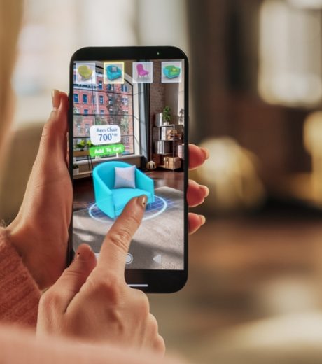 Decorating Apartment: Woman Holding Smartphone, using Augmented Reality Interior Design Software Chooses 3D Furniture for Home. Pick a Stylish Chair for the Living Room. Over Shoulder Close-up Screen
