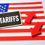 Tariffs text on blackboard with red arrows up and down over USA flag symbolizing trade war, customs duties, economic impact and international business policy.