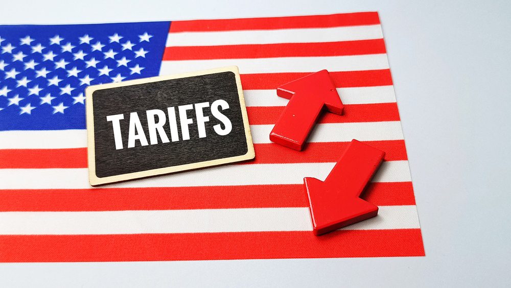 Tariffs text on blackboard with red arrows up and down over USA flag symbolizing trade war, customs duties, economic impact and international business policy.