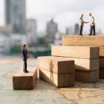 Miniature people: Successive business concept. Businessman thinking on first step of wood stair and two businessmen shaking hands on top step with modern city background