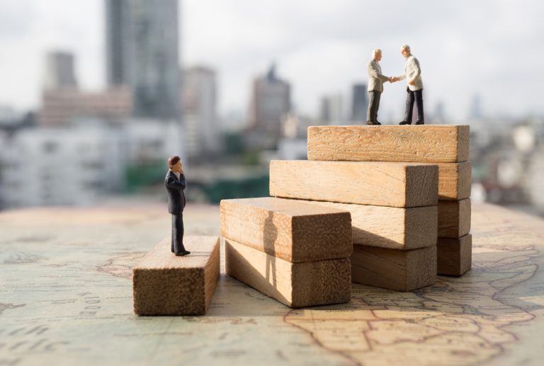 Miniature people: Successive business concept. Businessman thinking on first step of wood stair and two businessmen shaking hands on top step with modern city background